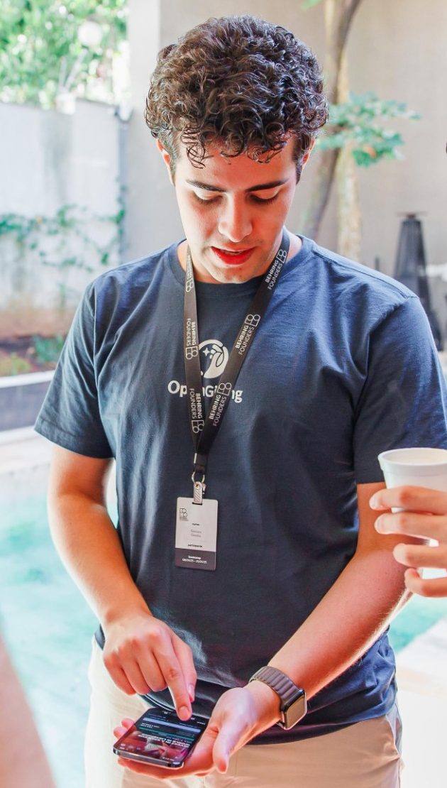 Enricco Gemha, in an OpenGiving T-shirt and a Behring Founders lanyard, demoing OpenGiving on his phone.
